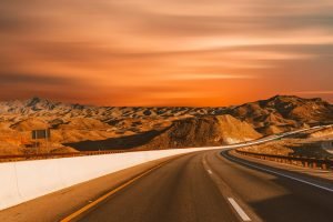 Empty highway winding through desert hills under a stunning sunset sky.